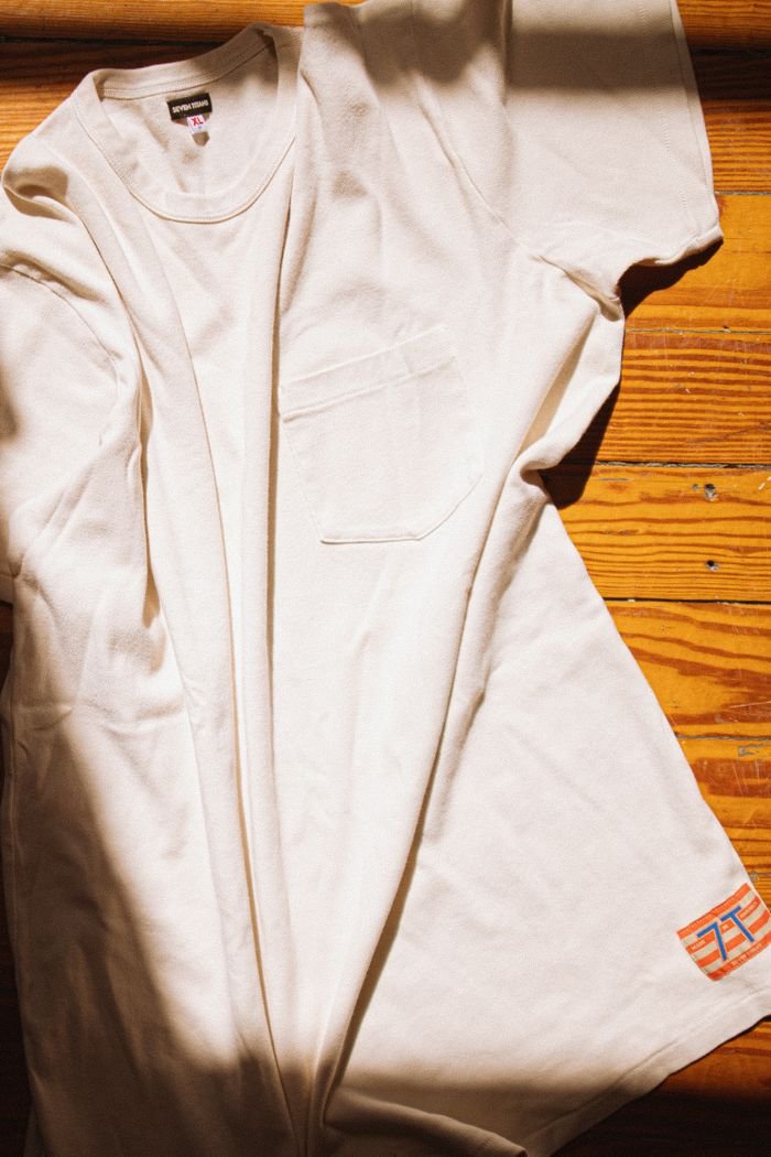 White cotton t-shirt laid on a wooden floor, captured in warm natural light, highlighting fabric texture.
