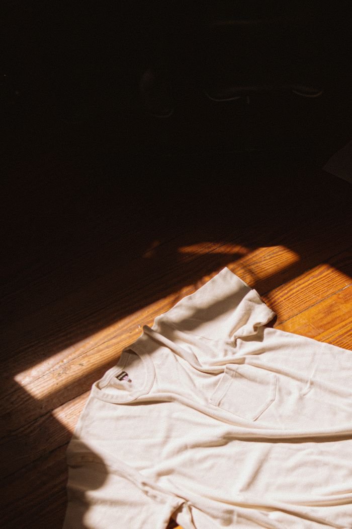White t-shirt on wooden floor illuminated by warm sunlight, showcasing fabric texture and minimalist style.