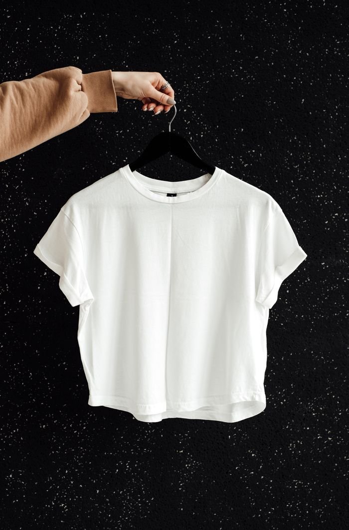 White t-shirt on hanger against a speckled black wall, showcasing minimalist fashion.
