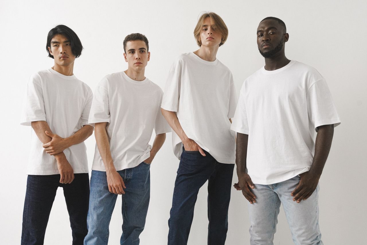 A group of four diverse men modeling white t-shirts and jeans in a studio setting.